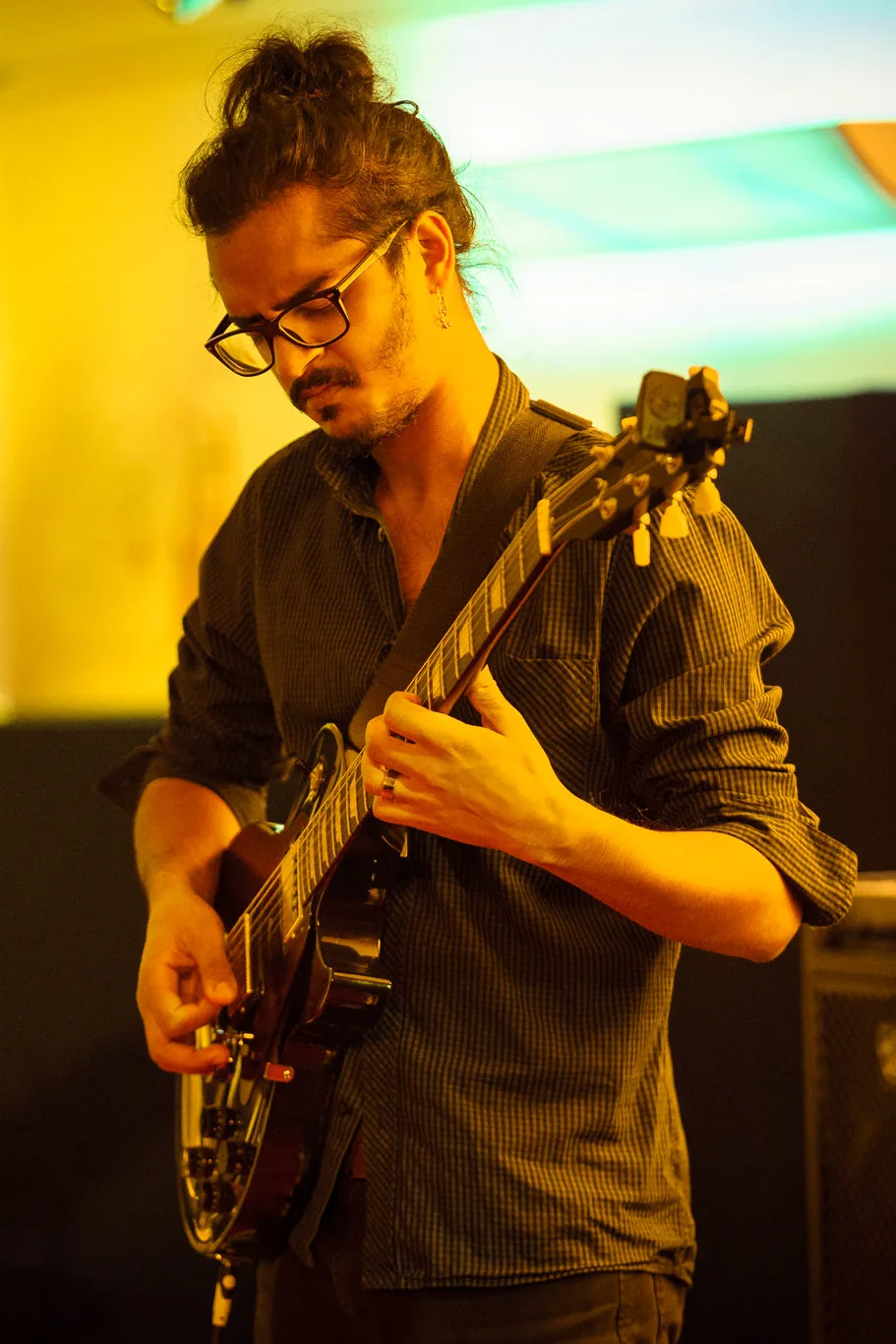 Close-up of Ravi Ramsahye playing electric guitar on stage under warm orange stage lighting