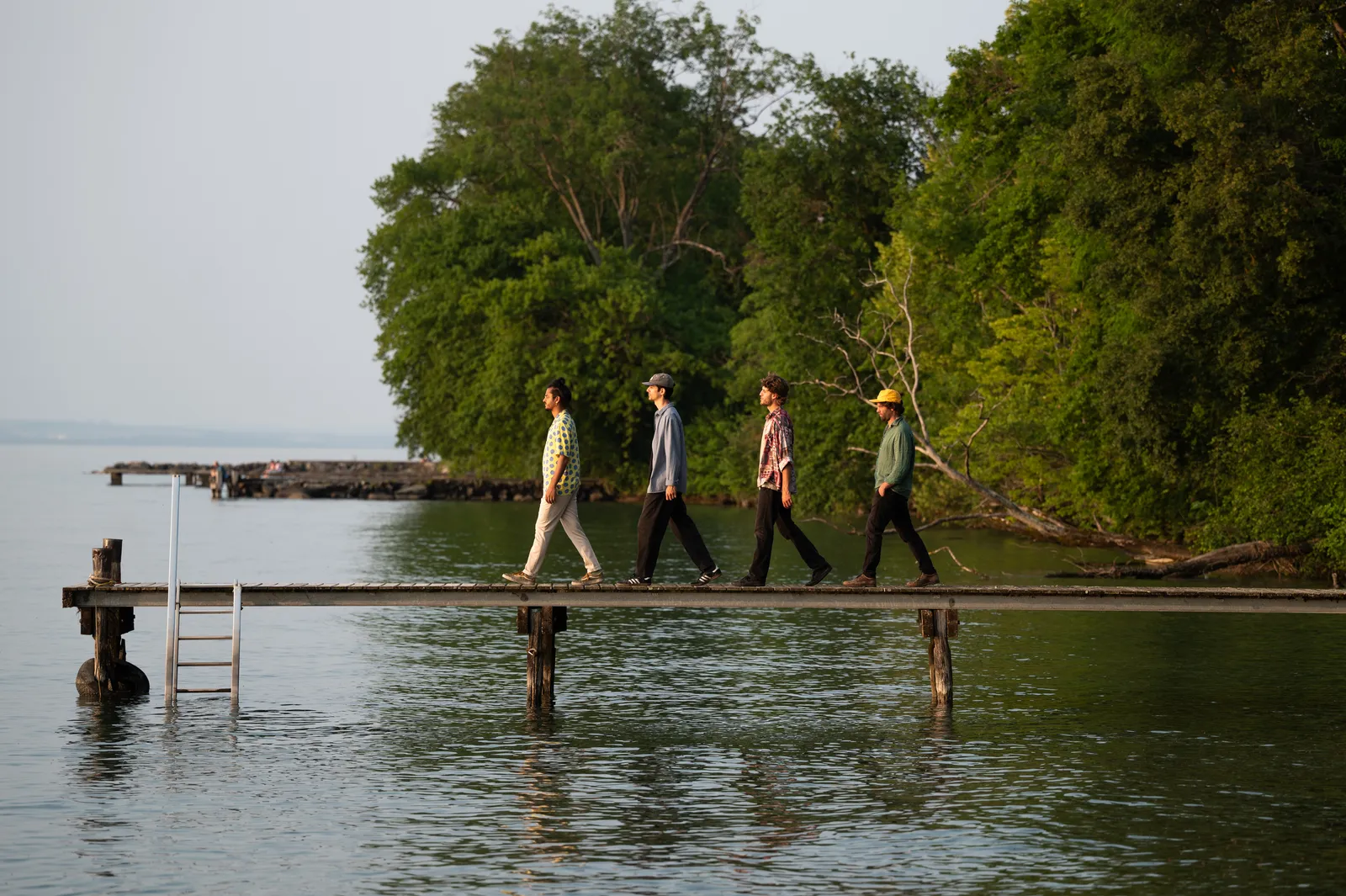 Wide view of the band walking a jetty beside a small wooded island on the lake