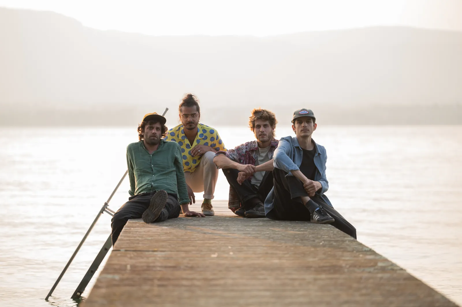 The four musicians sitting together at the end of a wooden pier, backlit by the setting sun